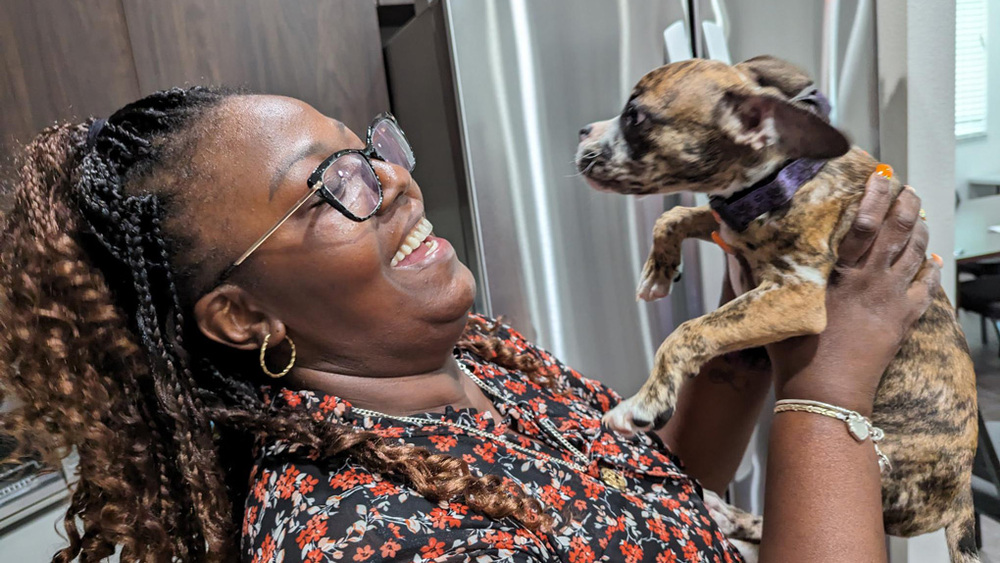 Woman smiling holding up puppy dog.