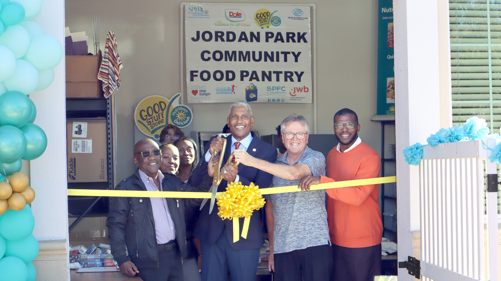 Group of officials about to cut a yellow ribbon at Jordan Park Community Food Pantry.