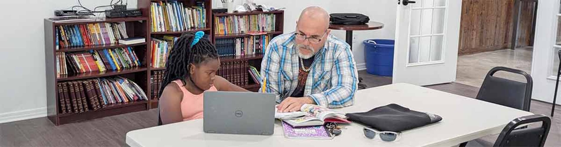 A man tutoring a girl using various notes, books, and a laptop.